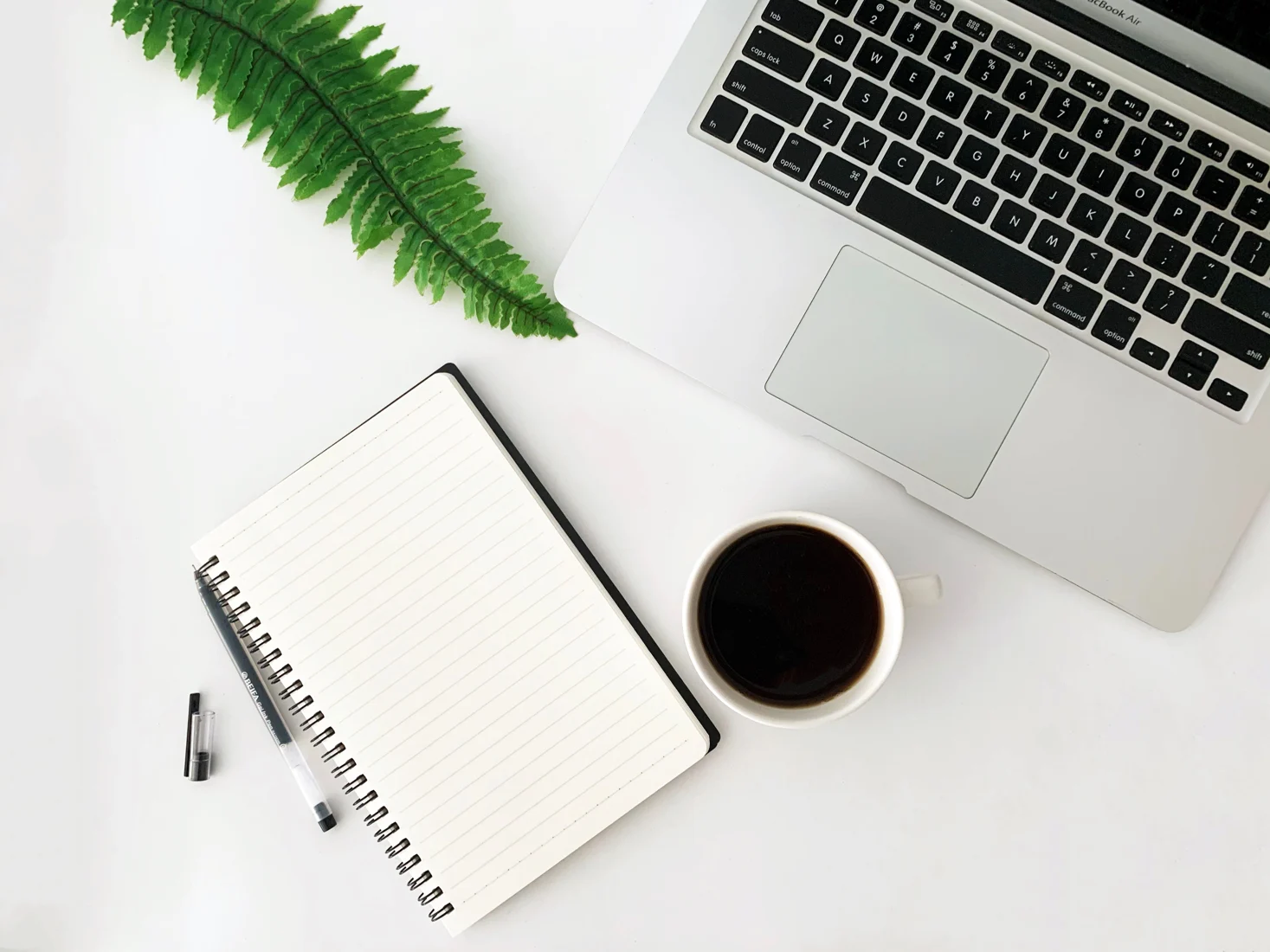 Offenes Notizbuch neben Laptop und Kaffeetasse