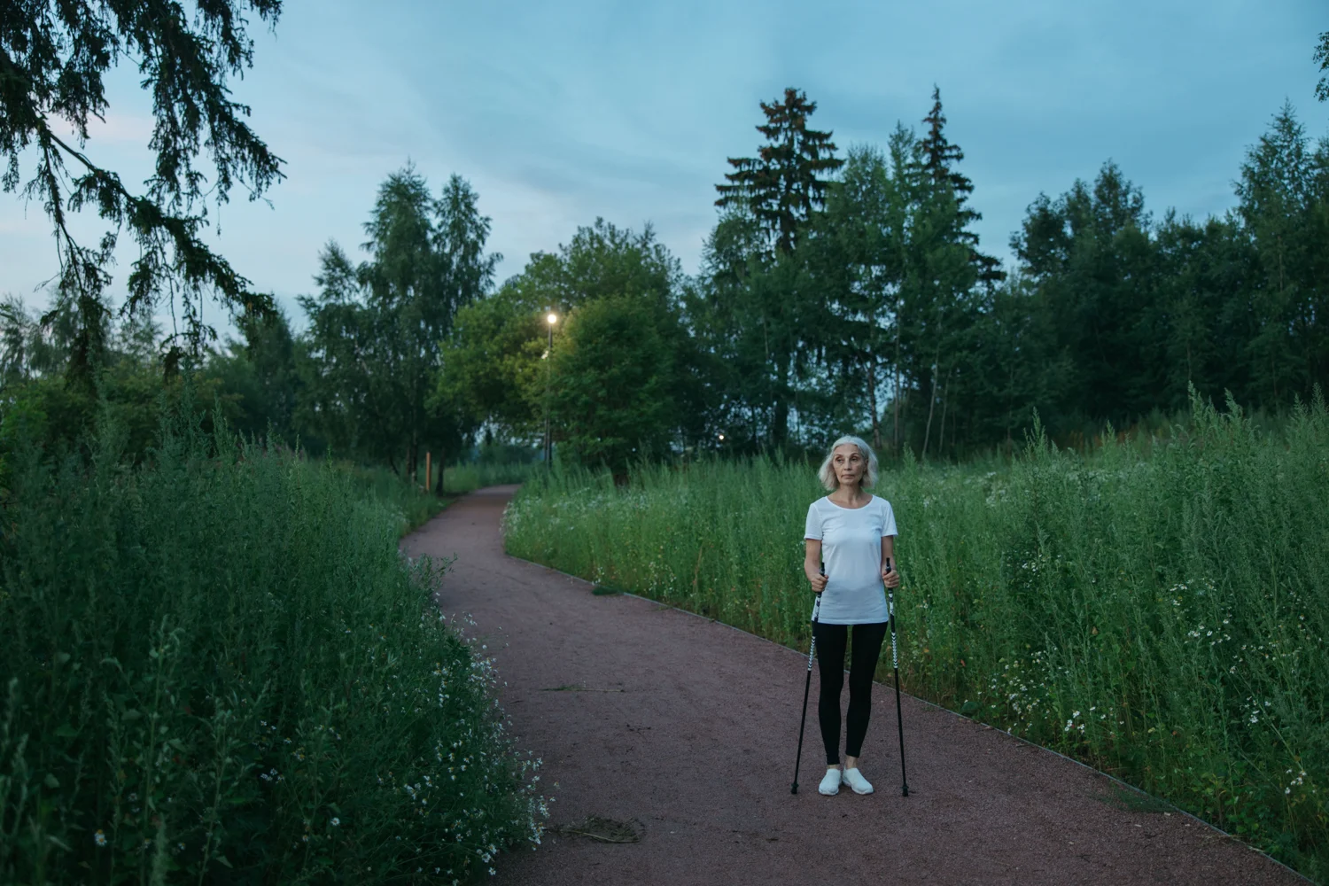 Frau mit Walkingstöcken auf einem Weg im Grünen